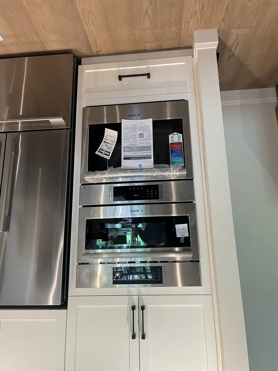 Two stainless steel wall ovens and a built-in microwave installed in a white cabinet column beside a stainless fridge