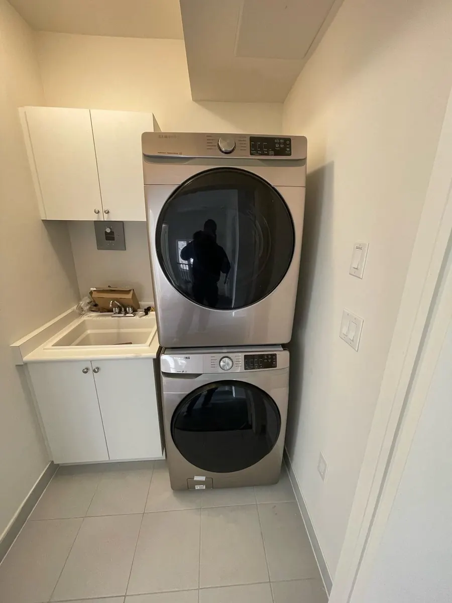Front-load washer and dryer stacked in a laundry room beside a utility sink